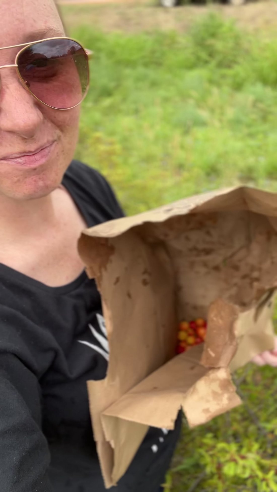 Kelsey holding open a brown paper sack with sand plums in the bottom